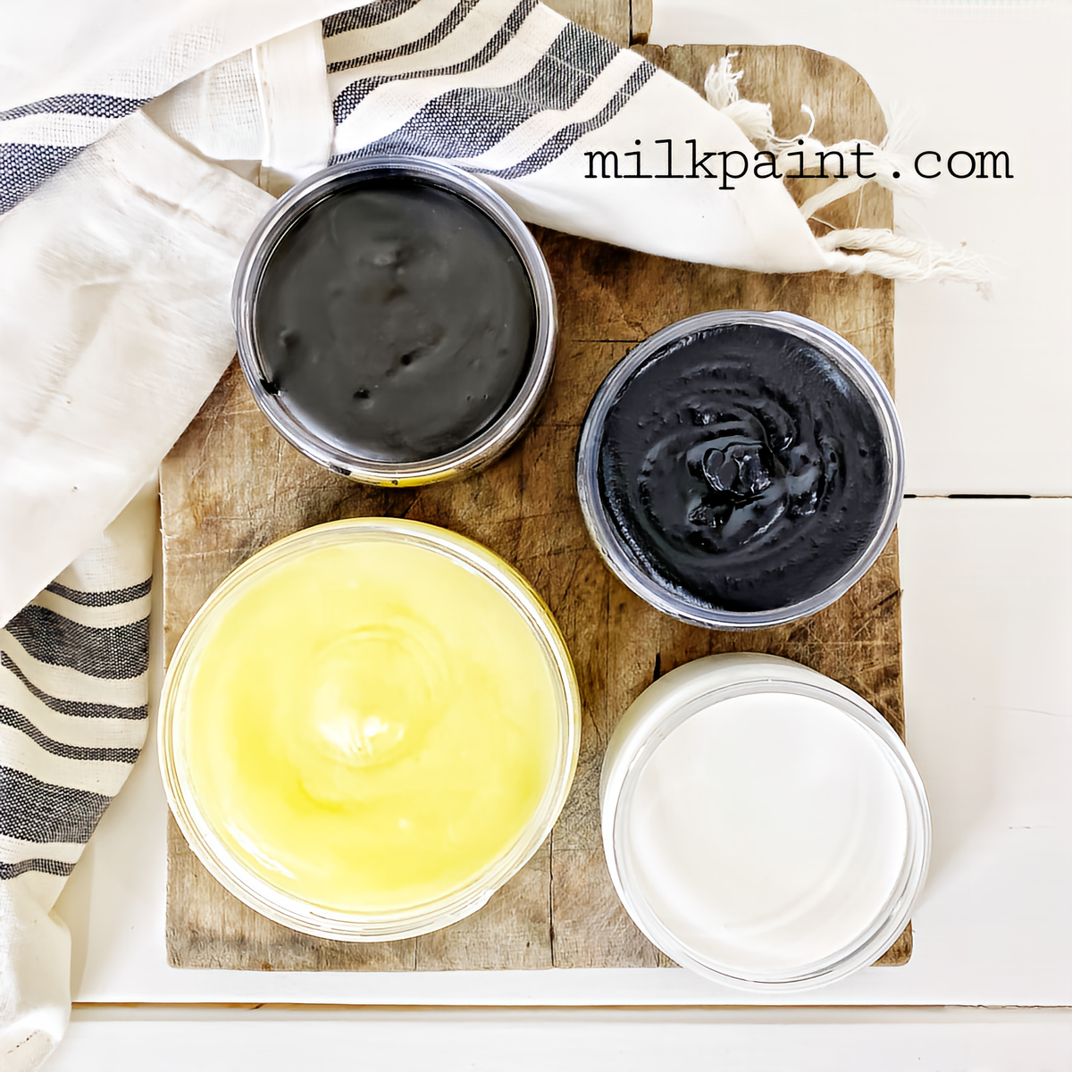 Four open paint jars with Black Beeswax Furniture Polish by Old Fashioned Milk Paint next to a striped towel.