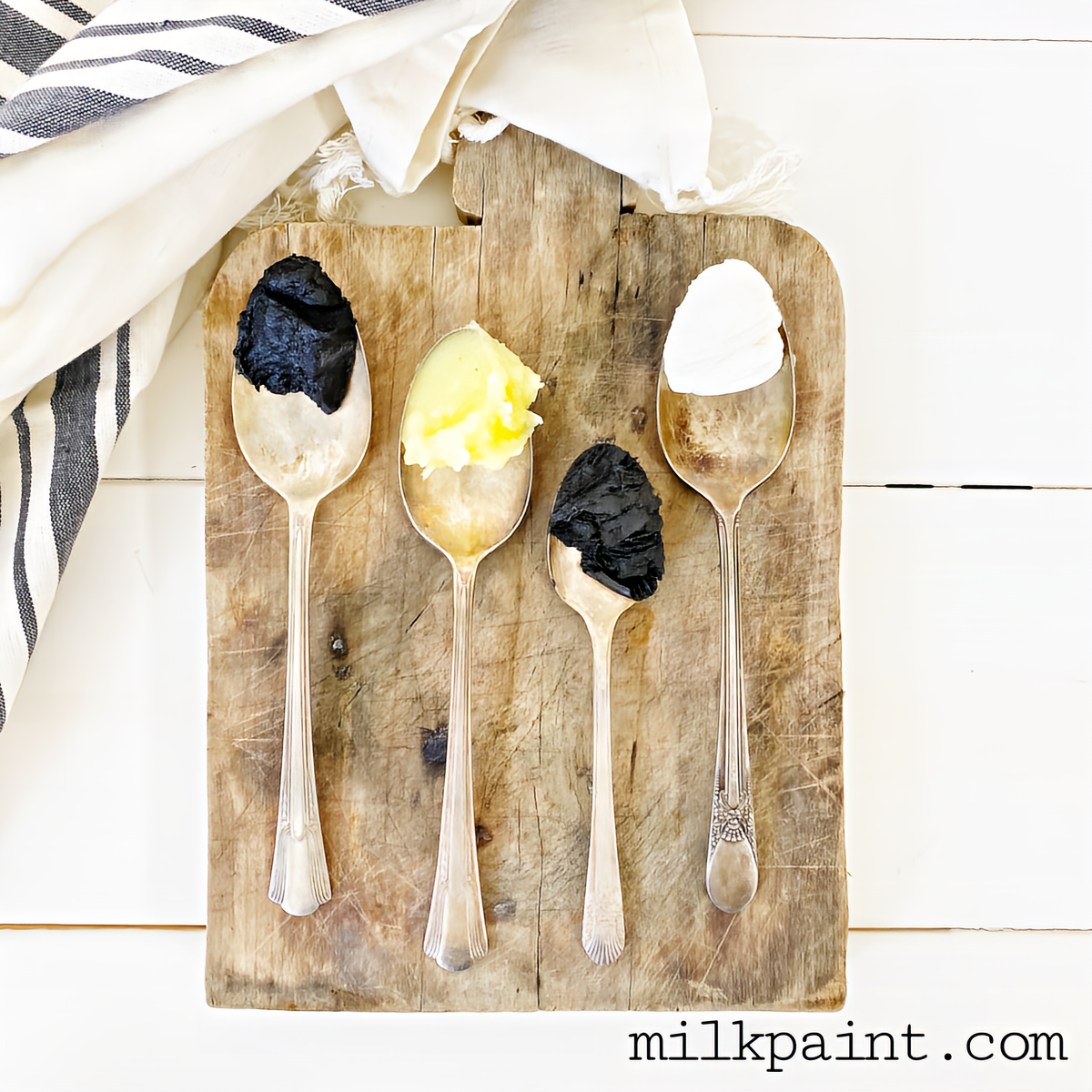 Four spoons with Black Beeswax Furniture Polish by Old Fashioned Milk Paint on wood surface, next to a cloth.