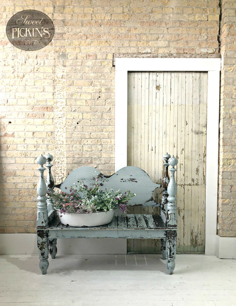 Bench painted in Bluebird by Old Fashioned Milk Paint holding flowers, shown against a brick wall and wooden door.