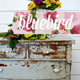 Distressed blue dresser with white knobs, floral bouquet, “Bluebird” pink fabric, painted in Old Fashioned Milk Paint.