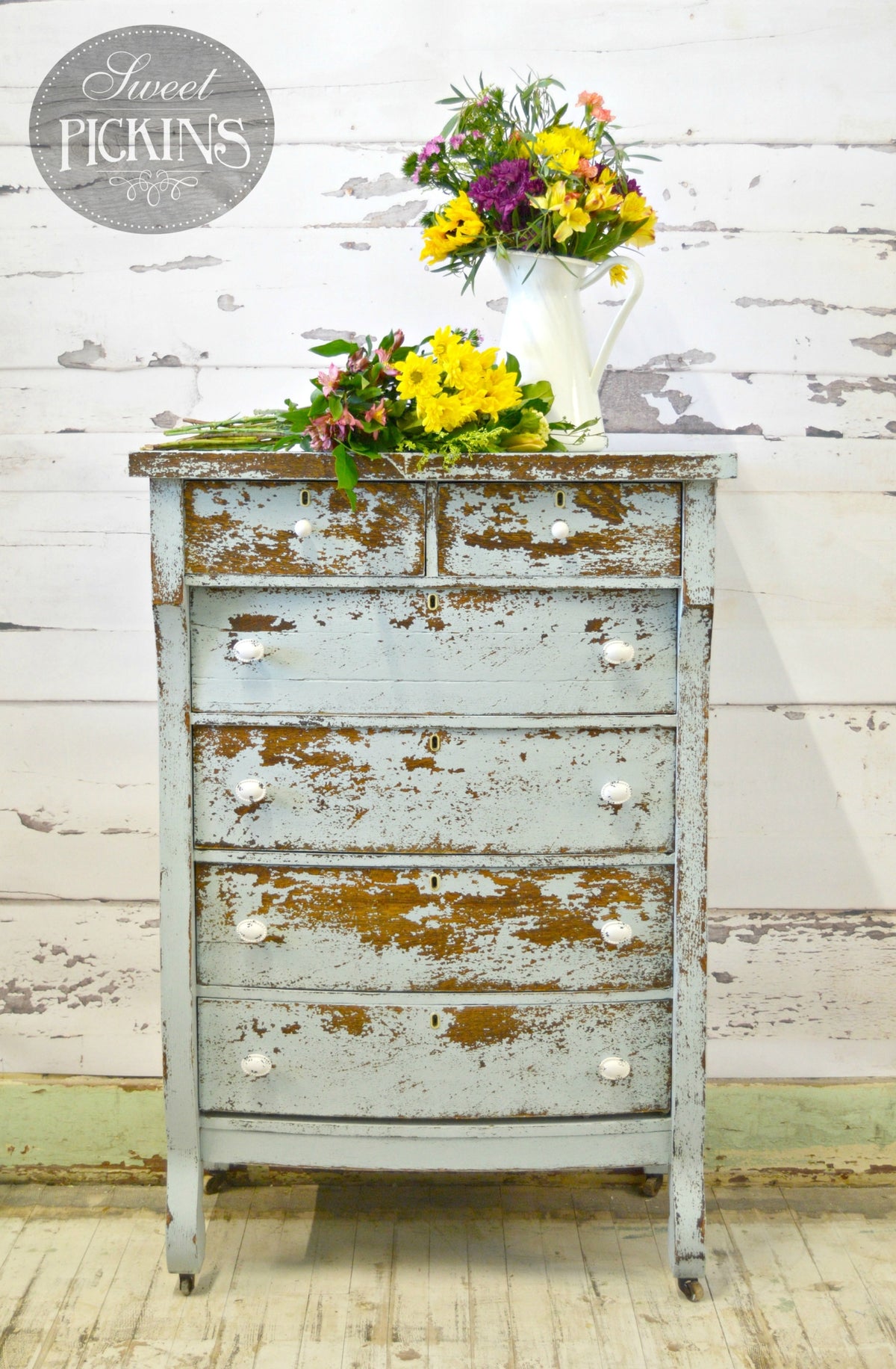 Distressed Bluebird dresser by Old Fashioned Milk Paint with white knobs, topped with yellow and purple florals.