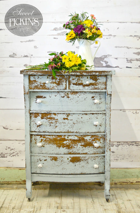 Distressed Bluebird dresser by Old Fashioned Milk Paint with white knobs, topped with yellow and purple florals.