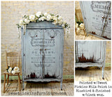 Bluebird armoire painted with Old Fashioned Milk Paint, black script, floral garland, and distressed edges.