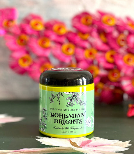 Bohemian Brights jar by DIY Paint Co. on a surface, pink flowers softly blurred in the background.