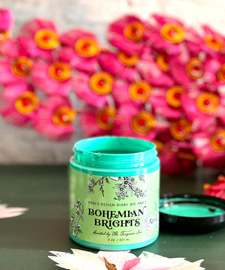 Bohemian Brights jar by DIY Paint Co. displayed on a table, pink and yellow flowers blurred in background.