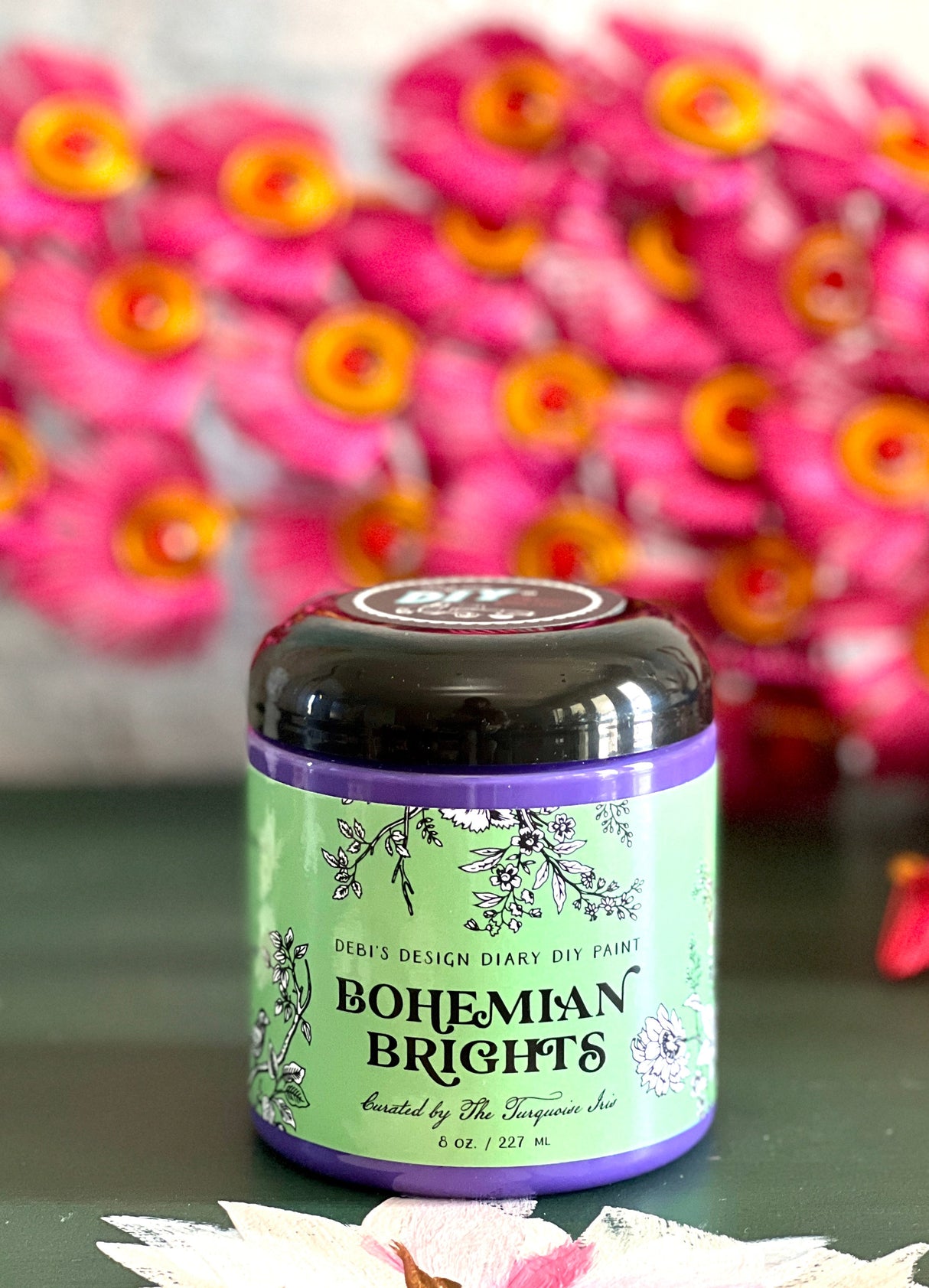 Bohemian Brights jar by DIY Paint Co. displayed on a surface, with blurred pink flowers in the background.