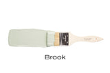 Paintbrush with Fusion Mineral Paint’s Brook, a vibrant blue-green shade, on a white background.