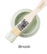 Brush with pale green Brook Fusion Mineral Paint resting on open Fusion Mineral Paint jar with label visible.