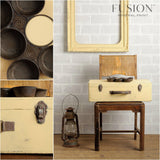 Suitcase painted in Buttermilk Cream Fusion Mineral Paint on chair; muffin tin, lantern, and frame nearby.