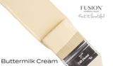 Paintbrush with creamy yellow bristles labeled “Buttermilk Cream Fusion Mineral Paint (Seasonal).”.