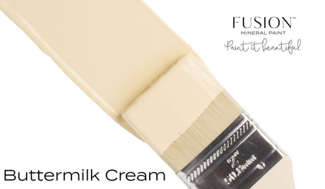 Paintbrush with creamy yellow bristles labeled “Buttermilk Cream Fusion Mineral Paint (Seasonal).”.