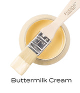 Open Fusion Mineral Paint Buttermilk Cream (Seasonal) jar with brush resting on top, bristles coated in yellow paint.