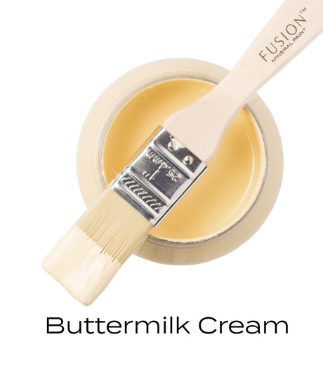 Open Fusion Mineral Paint Buttermilk Cream (Seasonal) jar with brush resting on top, bristles coated in yellow paint.