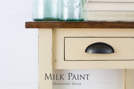 Cream table with dark wood top, decorated. Text reads: Buttermilk Cream Milk Paint by Homestead House.