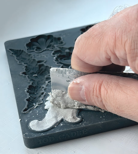 Hand smoothing plaster in a Cadré Mould by IOD, forming baroque frames on a white surface.