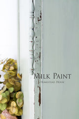 Distressed light green cabinet painted with Cartier Milk Paint by Homestead House; dried green flowers beside it.