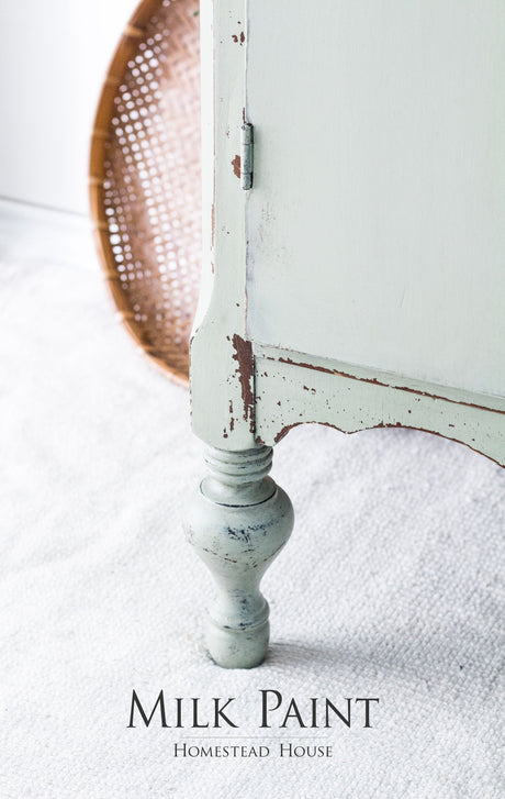 Distressed pale green table leg with Cartier Milk Paint by Homestead House branding below.
