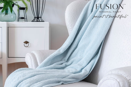 Blue blanket on white chair with black lamp, set against walls painted in Cashmere by Fusion Mineral Paint.