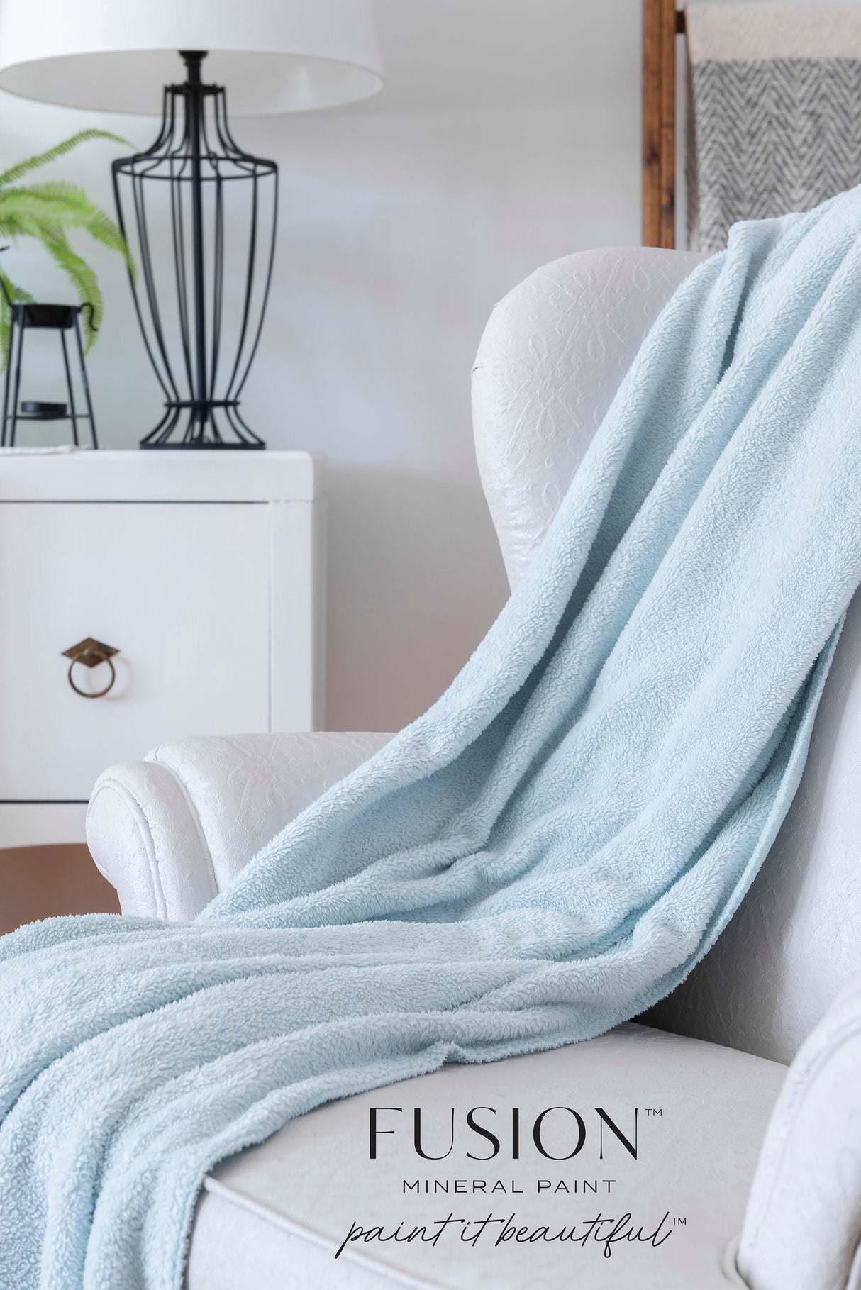 White chair with blue throw, set against Cashmere by Fusion Mineral Paint walls, beside a lamp and plant.
