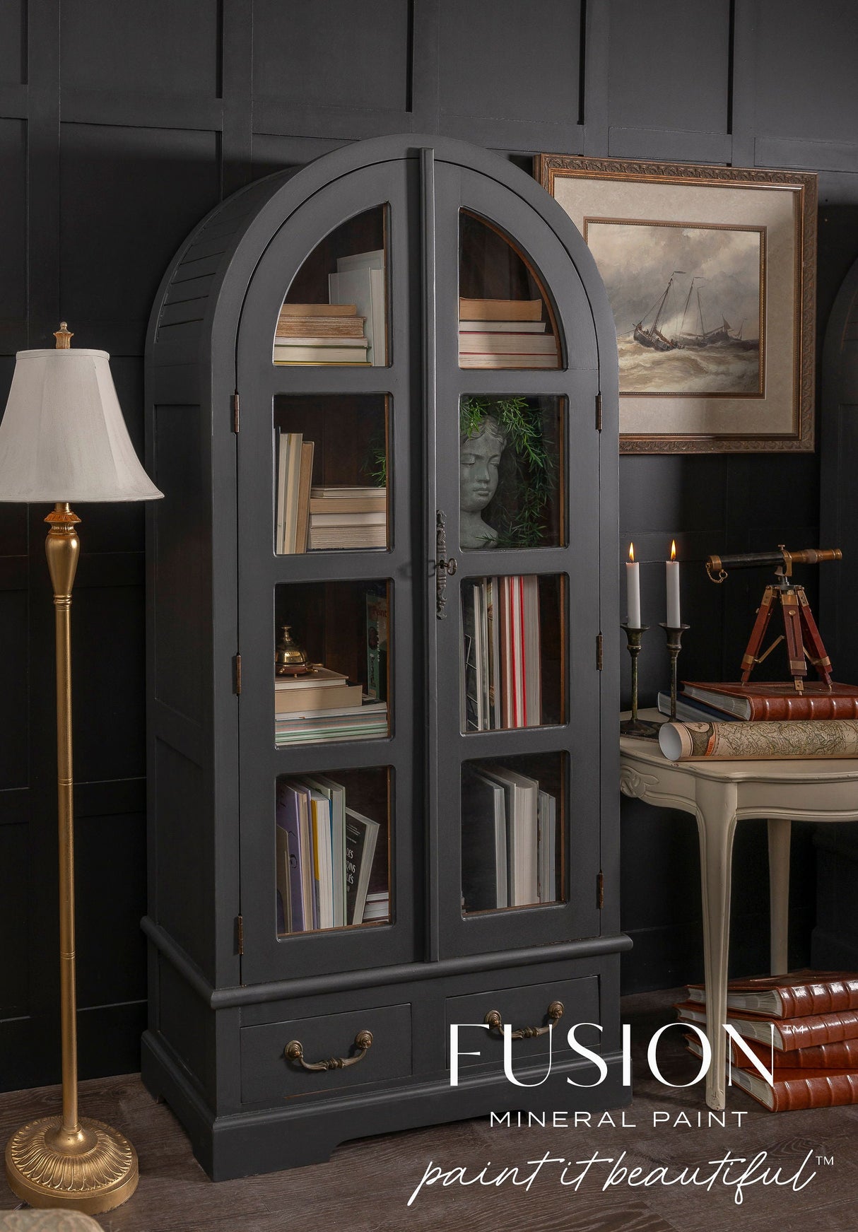 Dark gray arched glass cabinet in Fusion Mineral Paint Cast Iron, filled with books and decor, logo at bottom.