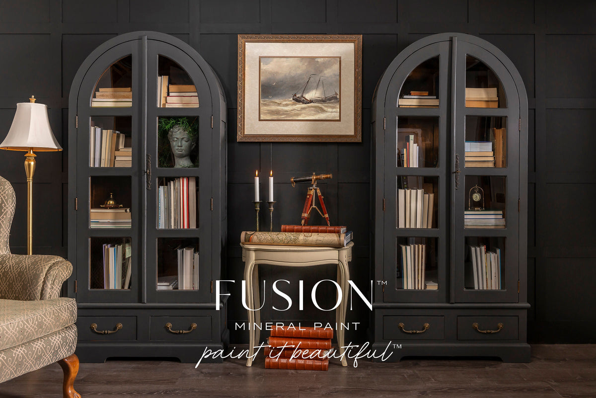 Two black arched bookshelves painted with Fusion Mineral Paint’s Cast Iron, displaying books and art.