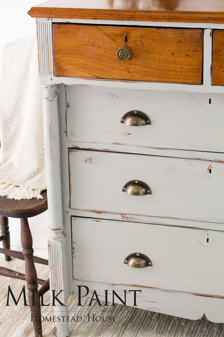 White wood dresser painted Cathedral Taupe Milk Paint by Homestead House, next to a brown chair and cream blanket.