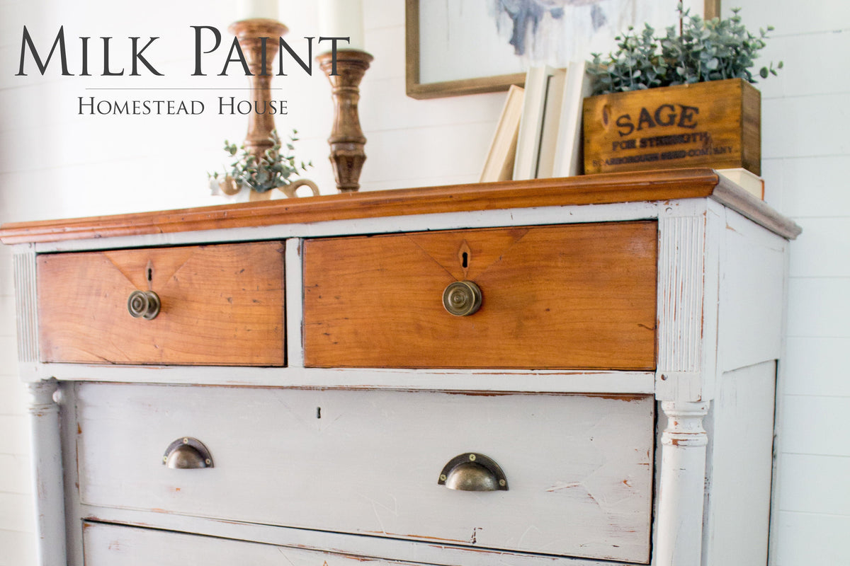 Partially painted Homestead House Cathedral Taupe dresser, two brown drawers, brass handles, candles on top.