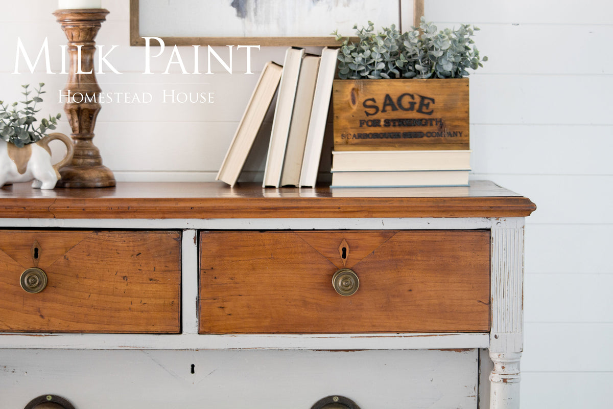 Dresser in Homestead House Cathedral Taupe Milk Paint with books and decor on top against a white shiplap wall.