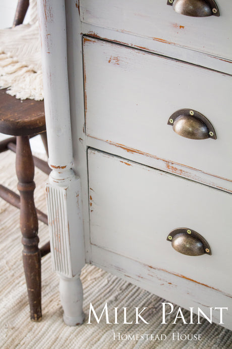 White dresser with metal cup handles, finished in Homestead House Cathedral Taupe Milk Paint, next to a chair.