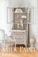 White desk with shelves, books, vases, and chair. Text: Cathedral Taupe Milk Paint by Homestead House.