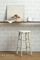 White stool on wood floor beneath shelf with teapot, pastries, and framed panel painted in Champlain Fusion Mineral Paint.