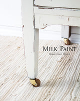Distressed white table leg in Champlain Milk Paint by Homestead House with brass caster wheels.