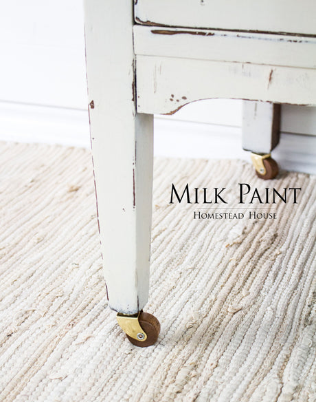 Distressed white table leg in Champlain Milk Paint by Homestead House with brass caster wheels.