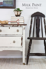Rustic chair and dresser in Homestead House Champlain Milk Paint beside books, plant pot, and toys on a rug.