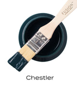 Brush with dark green Chestler Fusion Mineral Paint resting on open jar, matte finish visible on bristles.
