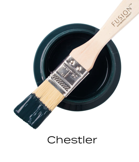 Brush with dark green Chestler Fusion Mineral Paint resting on open jar, matte finish visible on bristles.