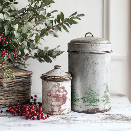 Two vintage metal canisters beside greenery, red berries, and a Christmas Wishes Stamp (2025) by I.O.D.
