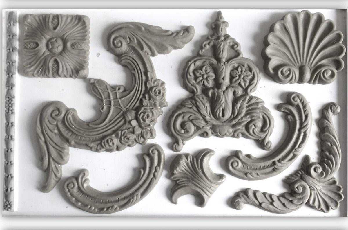 Gray plaster ornaments made with Classic Elements Mould by IOD on a plain background.