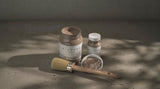 Three jars of Fusion Mineral Paint Clay Alchemy in taupe-gray shades with a brush nearby.