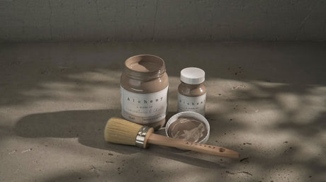 Three jars of Fusion Mineral Paint Clay Alchemy in taupe-gray shades with a brush nearby.