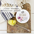 Clear Beeswax Furniture Polish by Old Fashioned Milk Paint next to wax on a board with a striped cloth nearby.