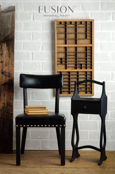 Black chair and side table with decor against a white brick wall painted in Fusion Mineral Paint Coal Black.