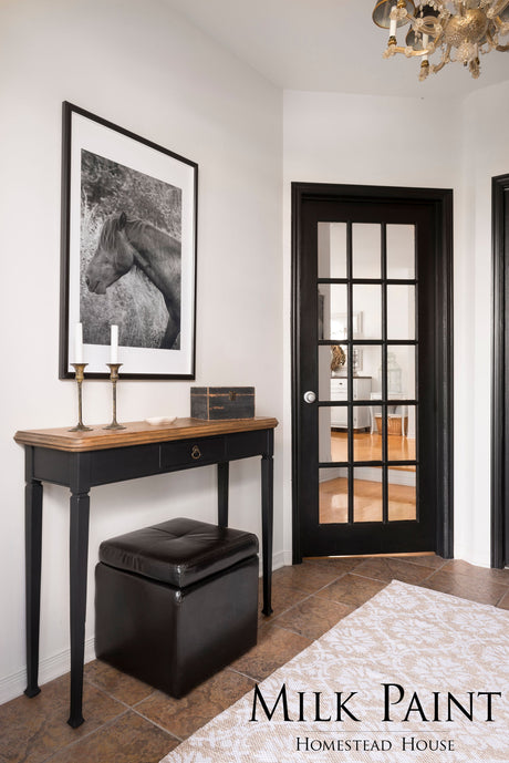 Entryway with Coal Black Milk Paint by Homestead House trim, wood console table, ottoman, and horse photo.