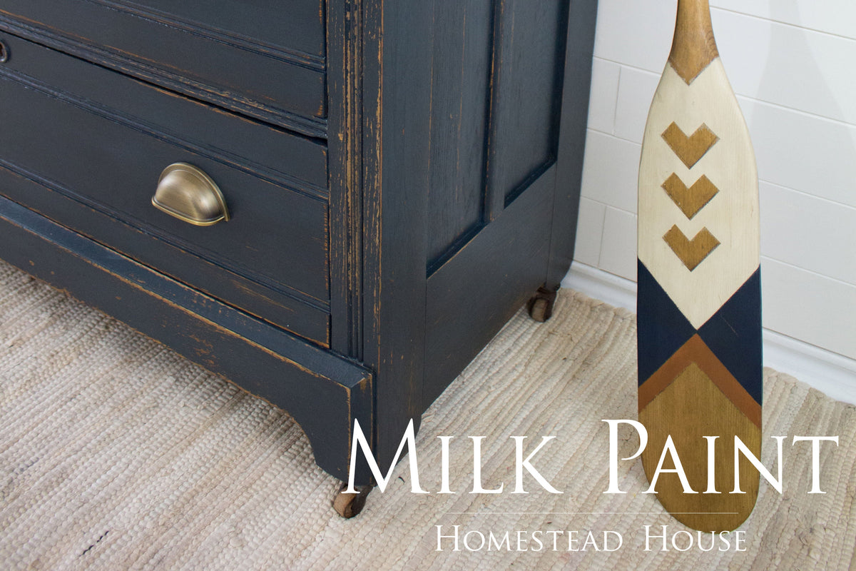 Blue dresser painted with Coal Black Milk Paint by Homestead House, shown next to a paddle on a rug.