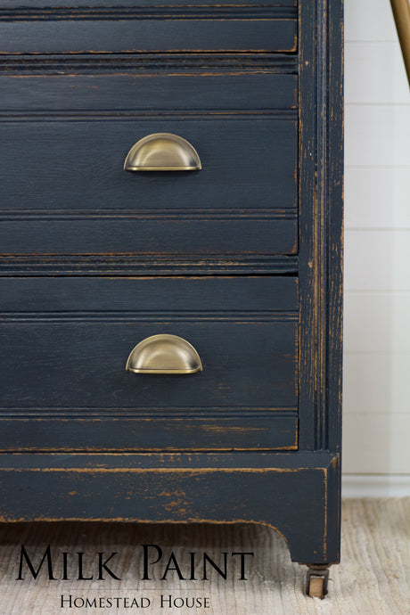 Navy blue dresser with brass pulls, distressed edges, and “Milk Paint” text; painted in Homestead House Coal Black.