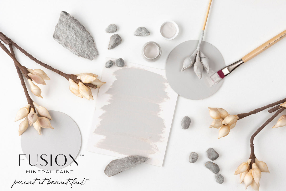 Fusion Mineral Paint Cobblestone, a warm grey, shown with rocks, brushes, and florals.