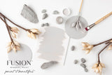 Fusion Mineral Paint Cobblestone, a warm grey, shown with rocks, brushes, and florals.