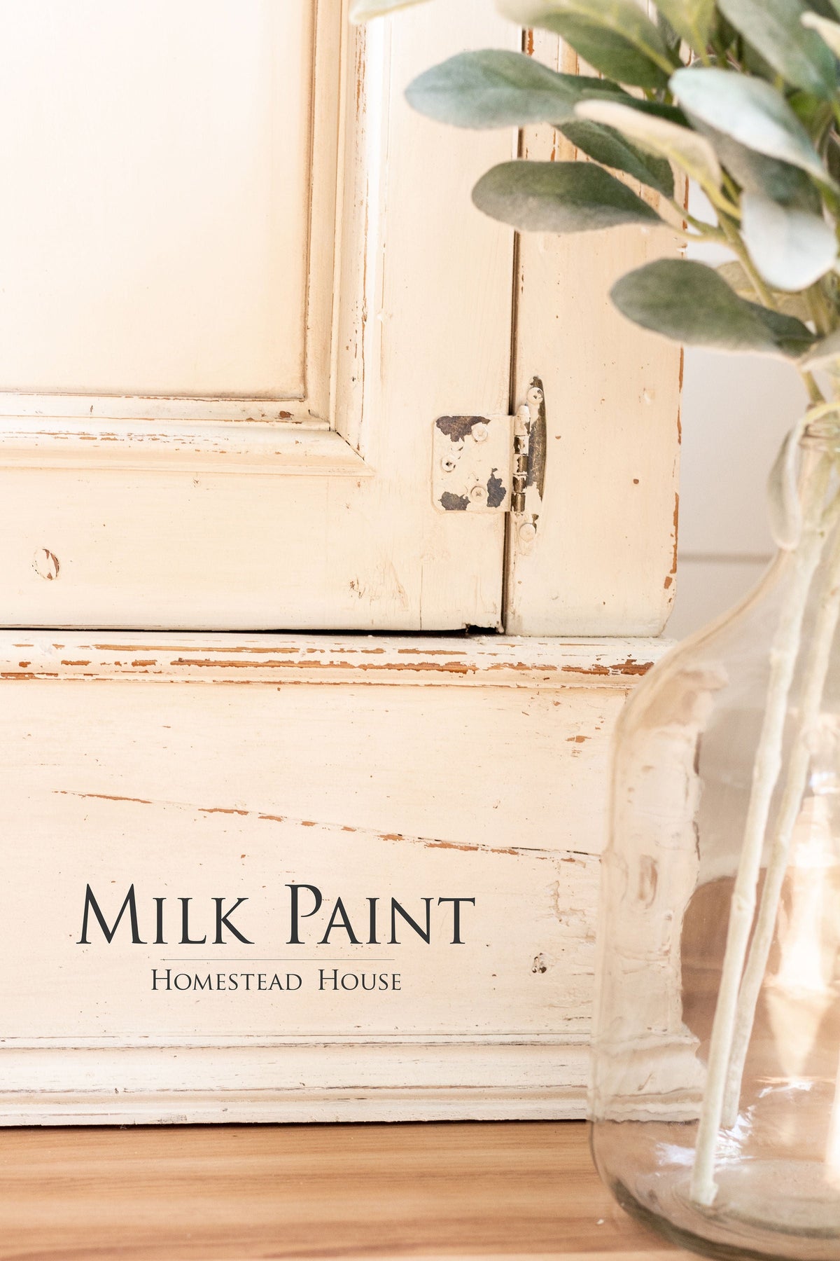 Distressed white cabinet in Combed Wool Milk Paint by Homestead House next to a glass vase with green leaves.