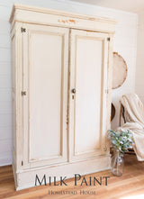 Cream-colored wardrobe painted in Homestead House Combed Wool Milk Paint, shown on wood floor.