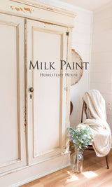 Cream armoire in Combed Wool Milk Paint by Homestead House, next to a chair with knit blanket and vase with greenery.